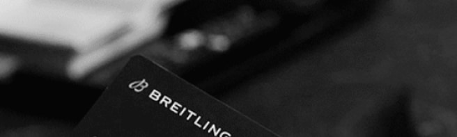 A male hand holds a Breitling warranty card with the inscription Chronomat B01 42.