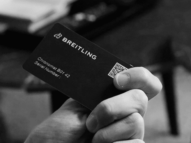A male hand holds a Breitling warranty card with the inscription Chronomat B01 42.