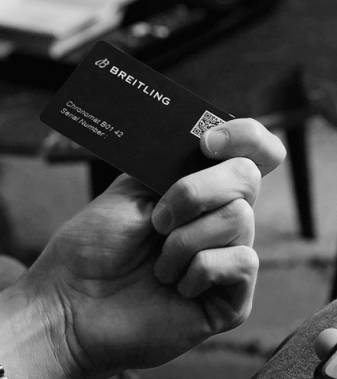 A male hand holds a Breitling warranty card with the inscription Chronomat B01 42.