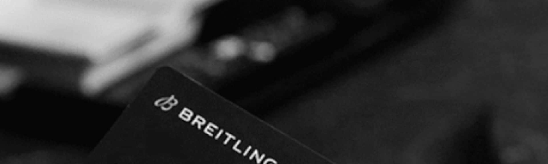 A male hand holds a Breitling warranty card with the inscription Chronomat B01 42.