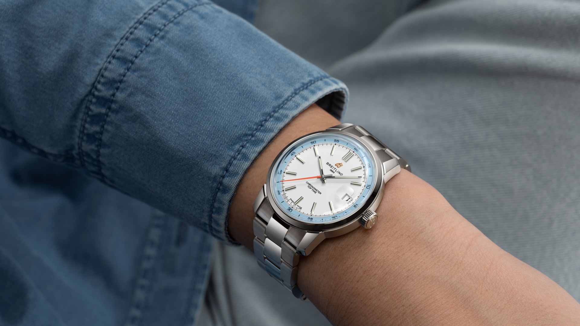 {generated} ブライイトリングTop Time B31が手首に映え、シルバーダイヤルと青の差し色、スチールブレスが穏やかな雰囲気を演出。