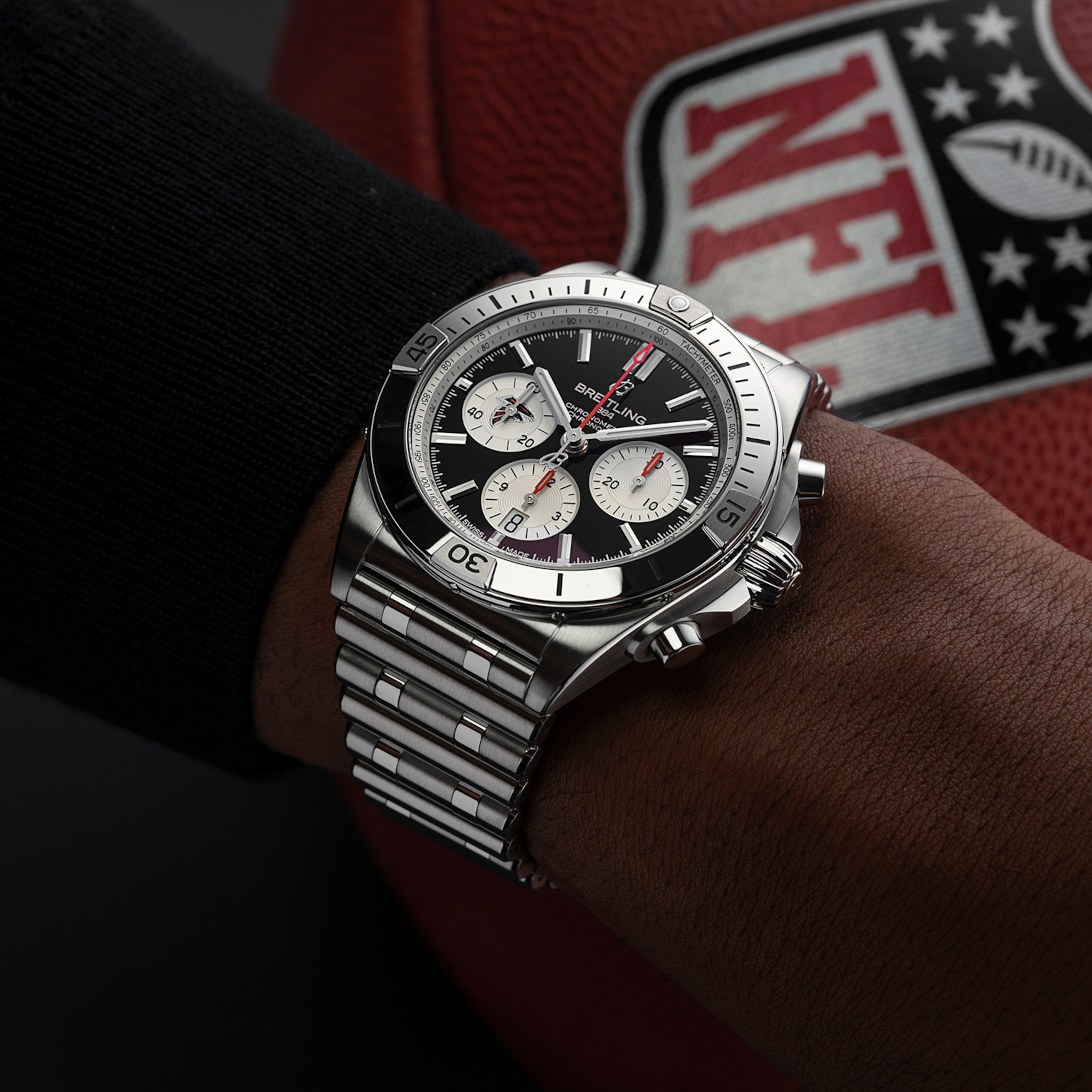 Limited edition NFL watch with red dial on the wrist, in the background is a football with an NFL logo.