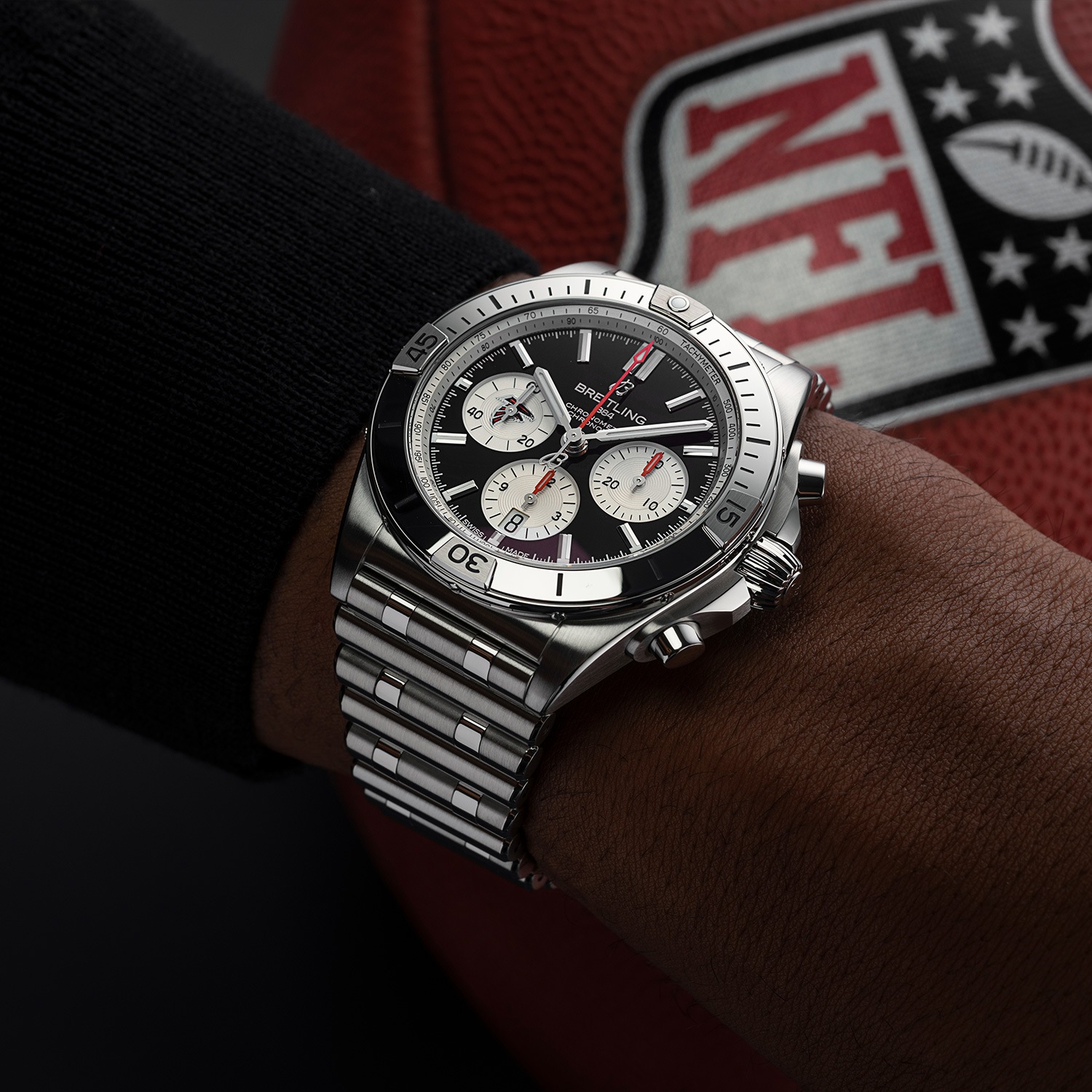 Limited edition NFL watch with red dial on the wrist, in the background is a football with an NFL logo.