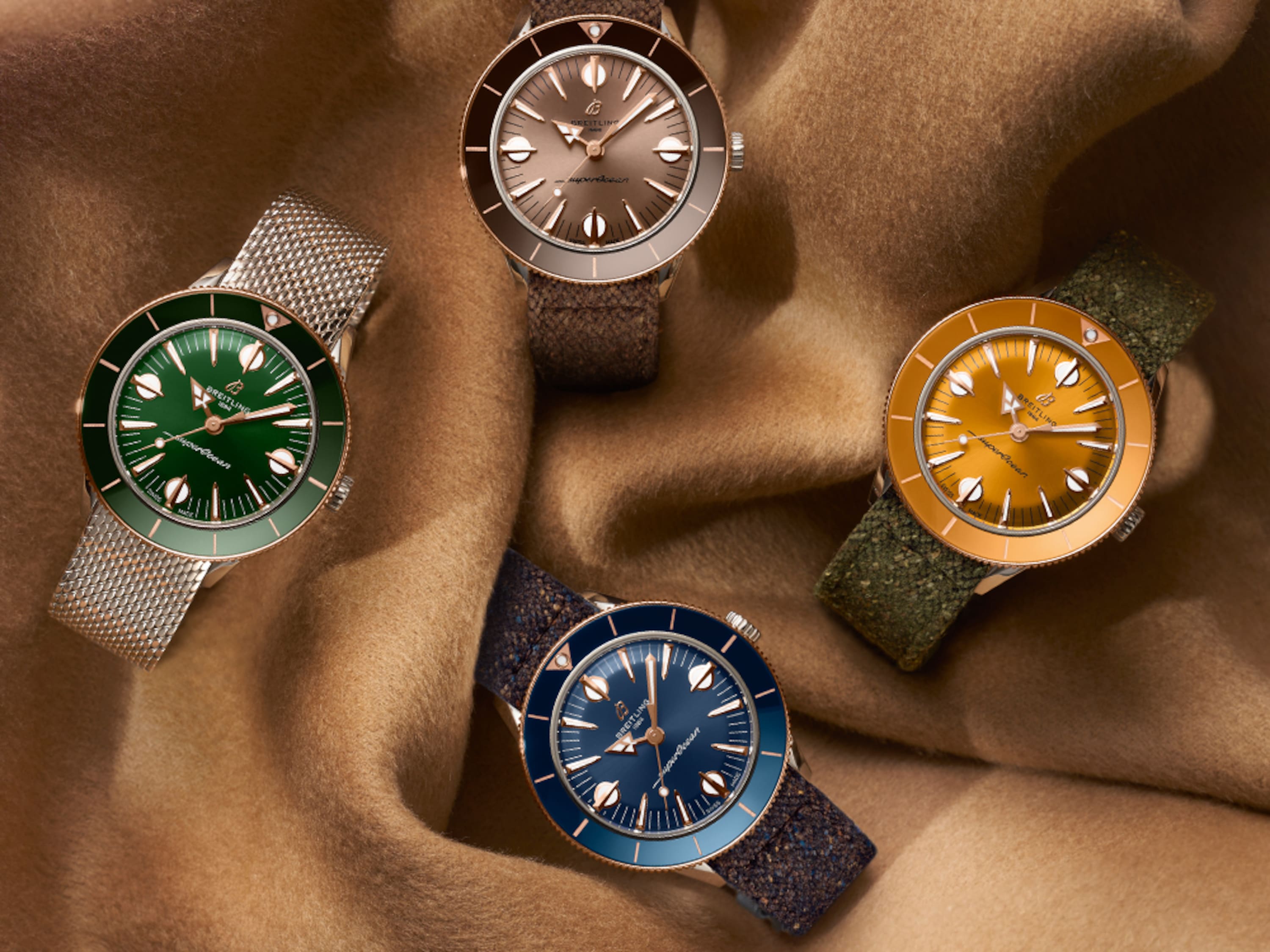 Cuatro relojes Superocean Heritage de diferentes colores descansan sobre una tela marrón.