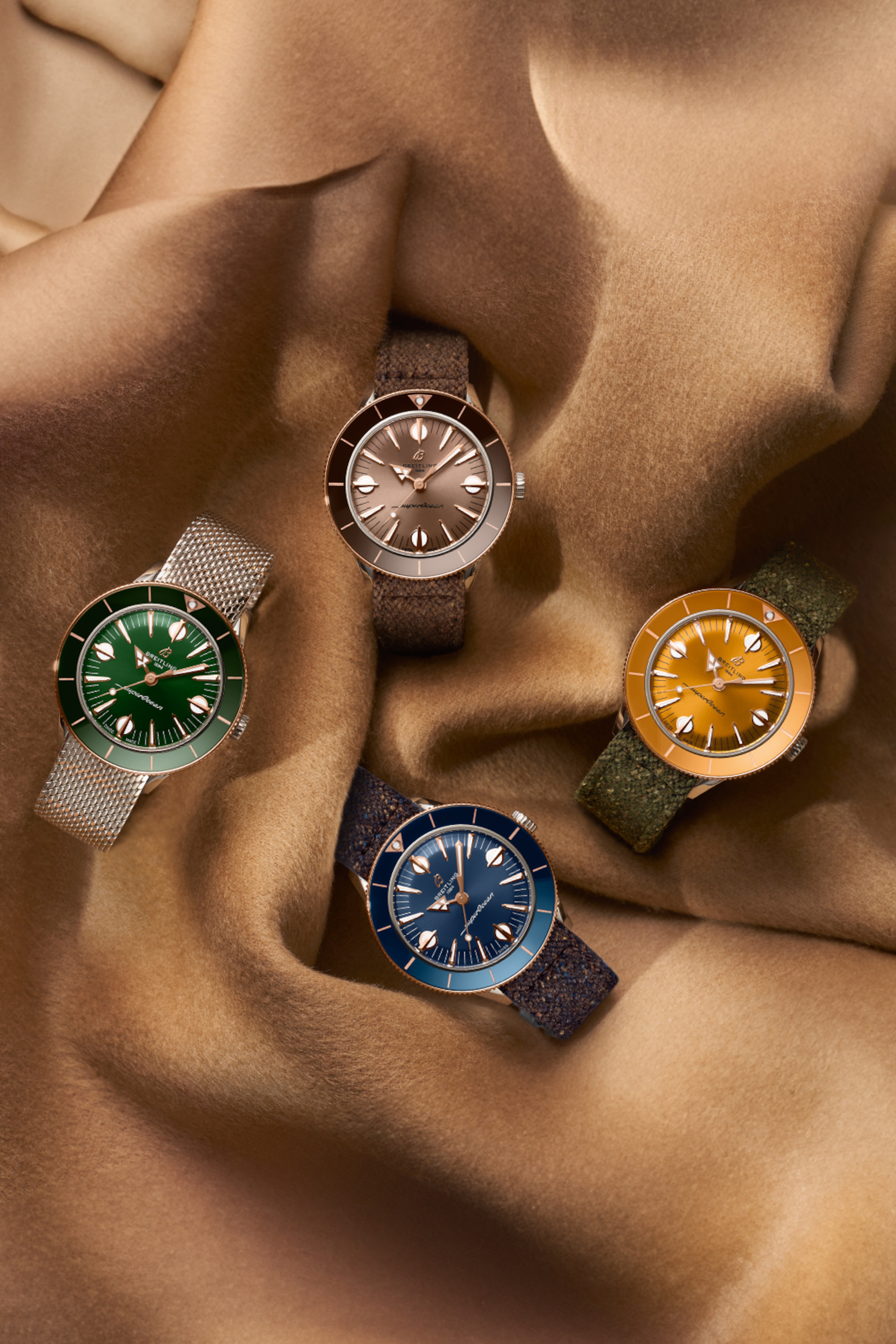 Cuatro relojes Superocean Heritage de diferentes colores descansan sobre una tela marrón.
