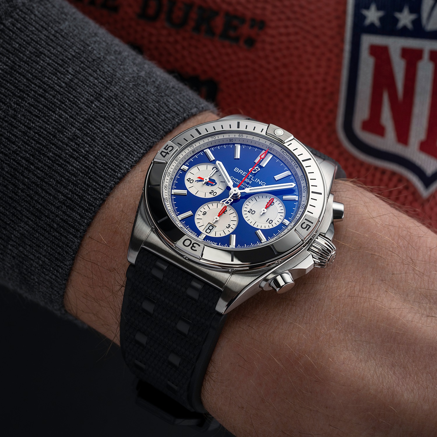 A male hand with a blue Chronomat B01 42 NFL Team Editions holds a football.