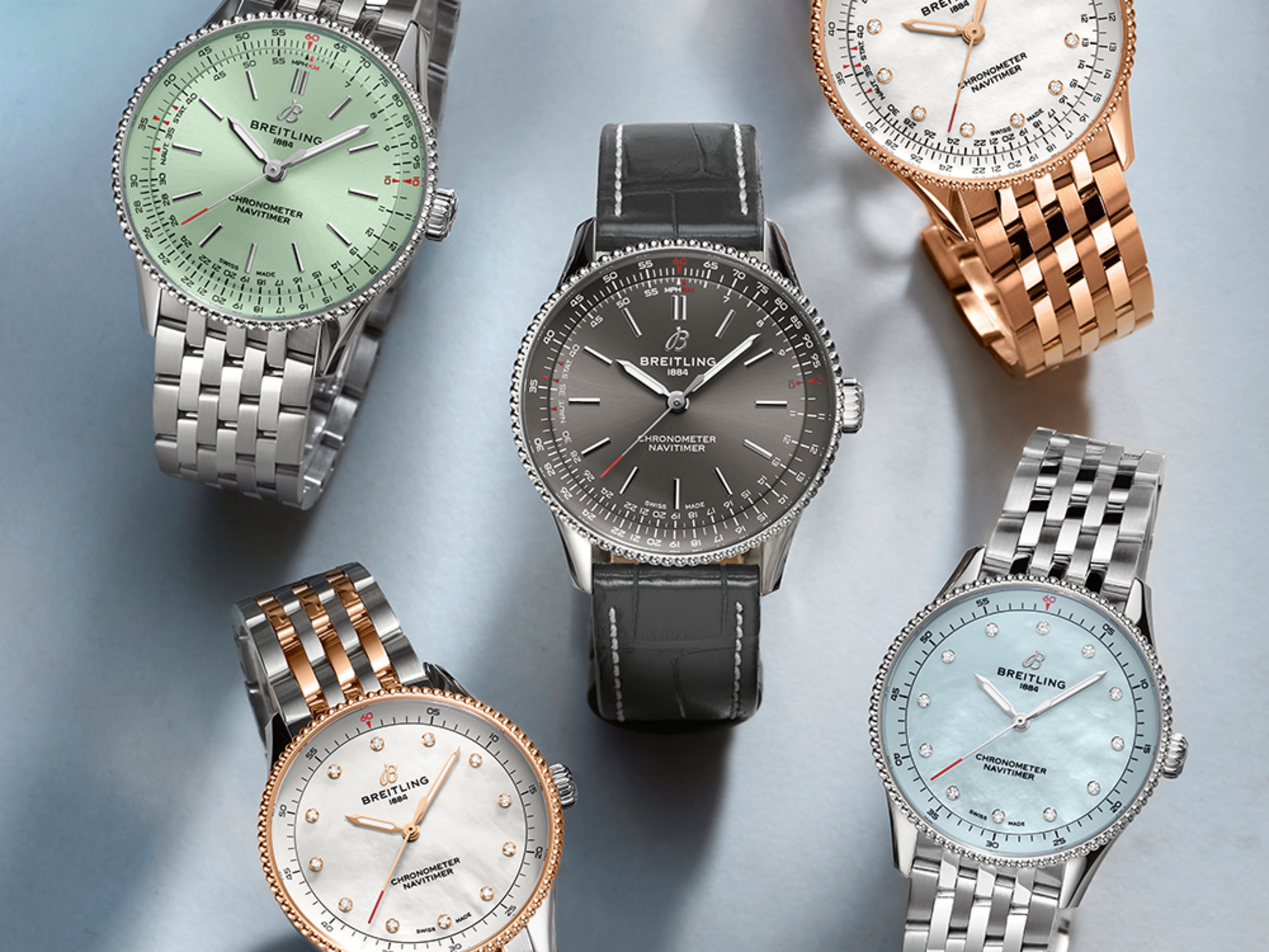 Five Navitimer watches with different-colored dials lie on a blue cloth.