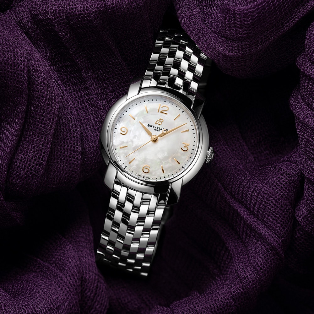 {generated} Breitling Lady Premier A77330121A2A1 en acero pulido con esfera blanca presentada sobre un fondo de tela púrpura