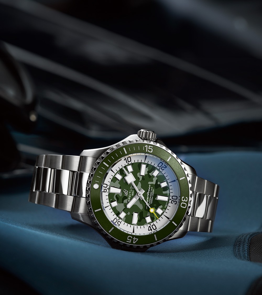 {generated} Breitling鈦金屬腕錶以綠色迷彩錶盤與鋼錶鏈置於深色裝備上，展現其堅固而精準的特質。