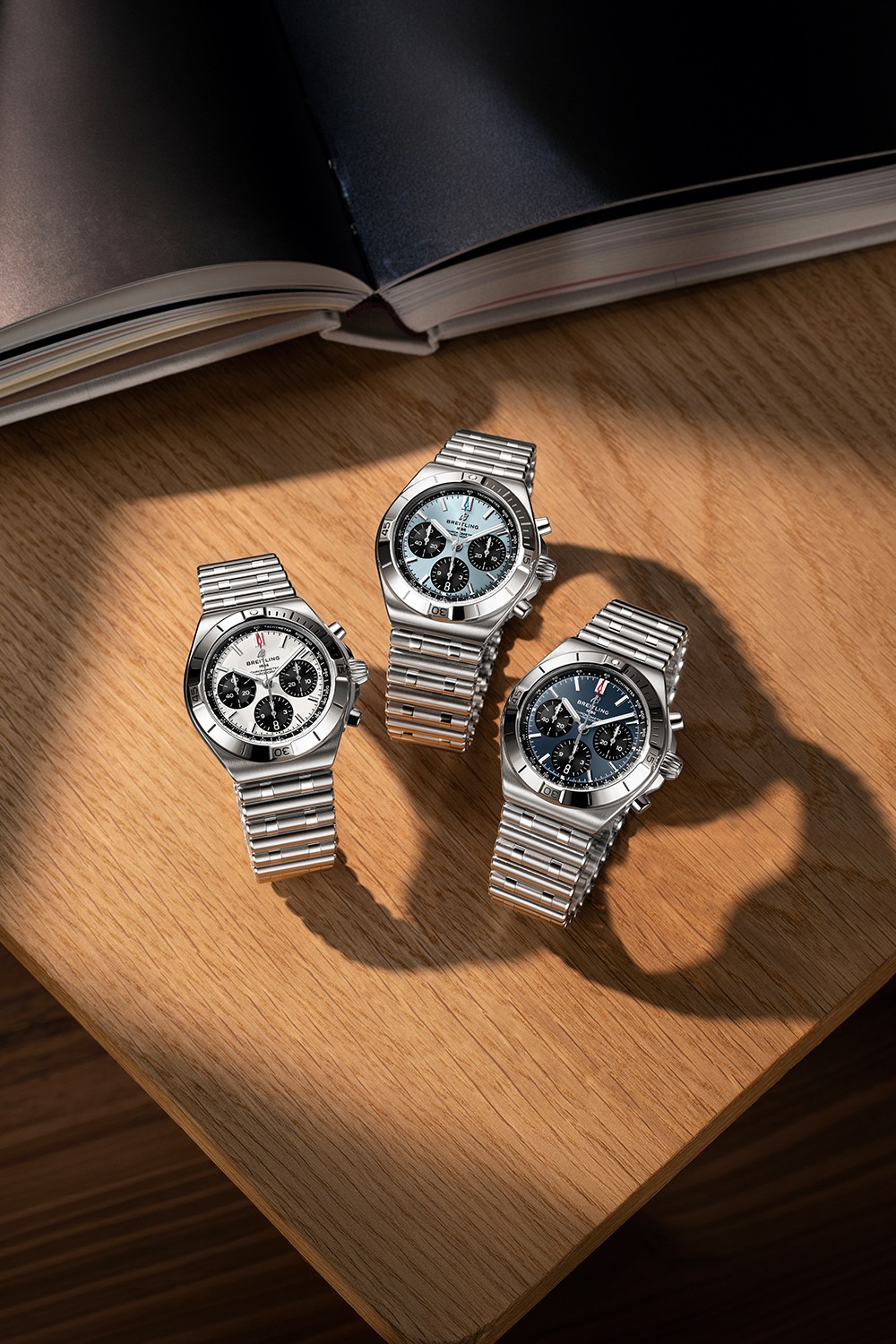 A gold and a silver Chronomat with dark green rubber straps on a brown table.