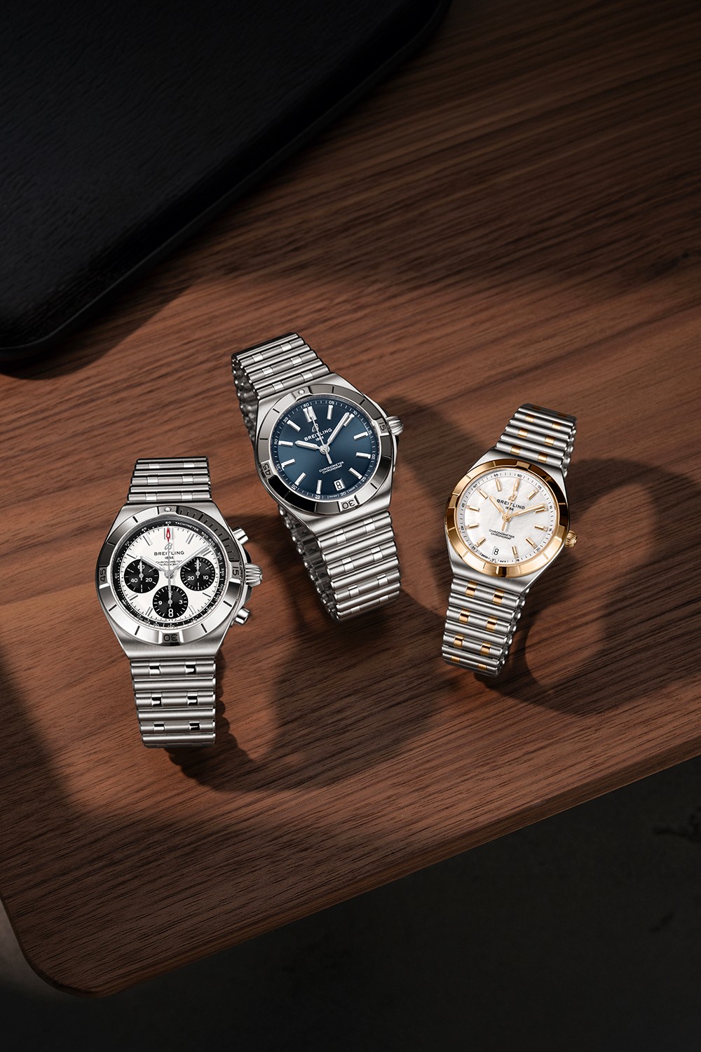 Three silver and three gold Chronomat watches with different-colored dials against a black background.