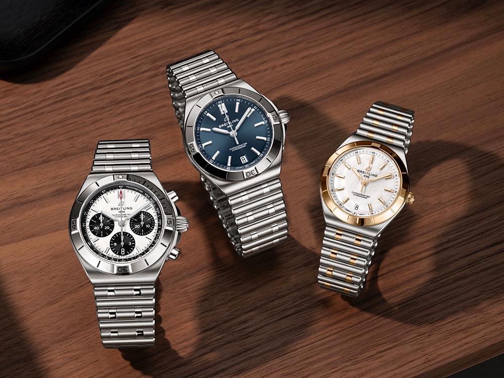 Three silver and three gold Chronomat watches with different-colored dials against a black background.