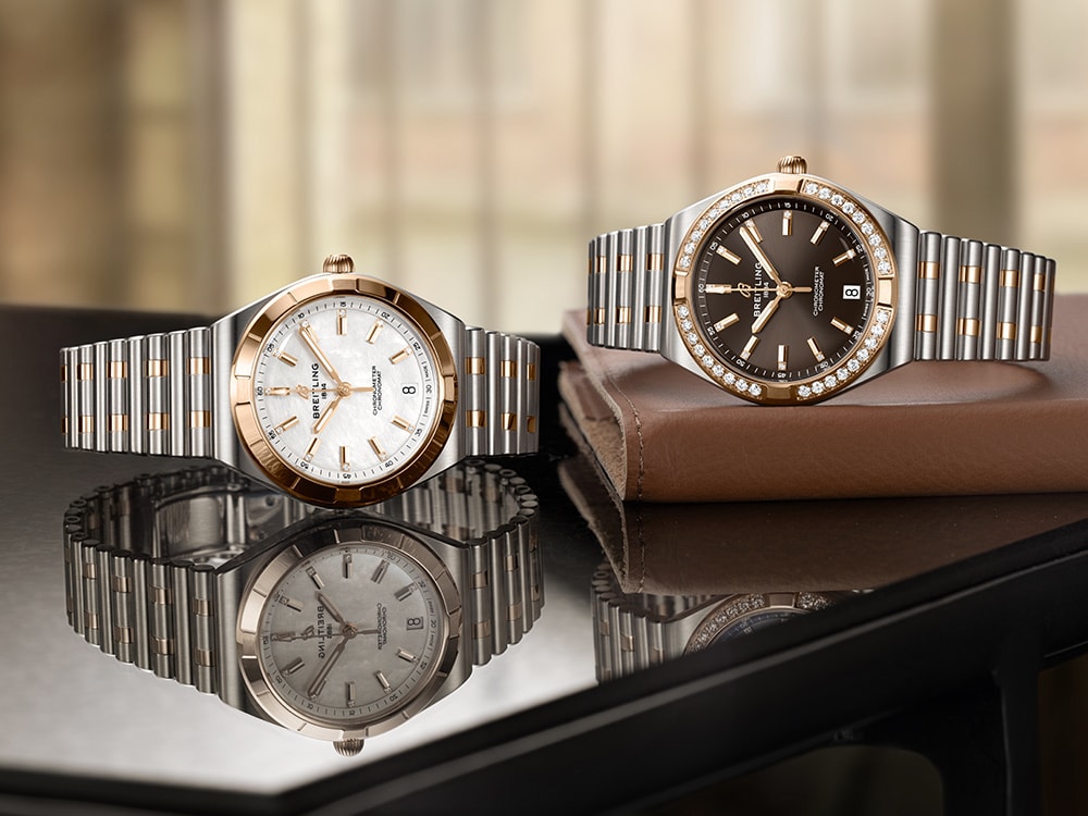 Three silver and three gold Chronomat watches with different-colored dials against a black background.