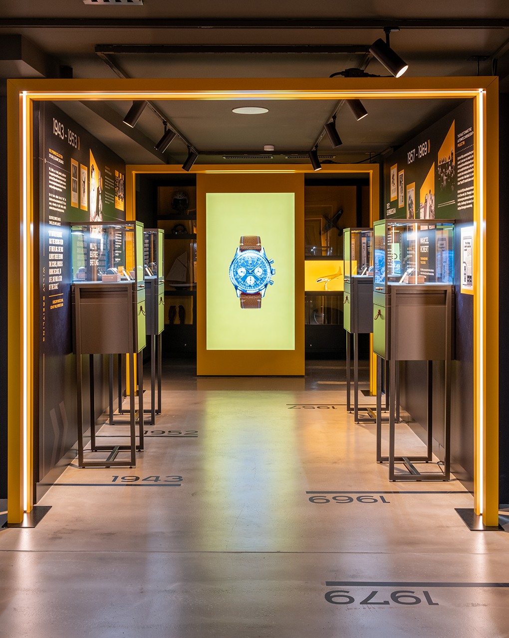 {generated} A museum-style gallery presents Breitling heritage with a central screen highlighting a Breitling watch against a yellow backdrop.