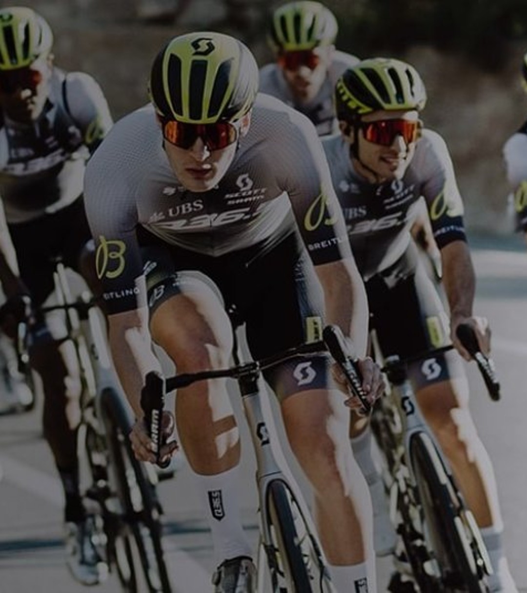 {generated} 身著統一隊服並帶有Breitling標識的車隊在陽光照耀的彎道路段整齊前進。