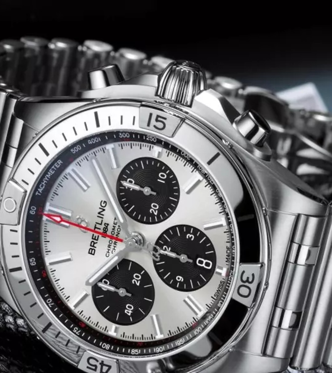 {generated} Полированный стальной хронограф Breitling Chronomat рядом с винтажной камерой, подчёркивая выразительный циферблат и браслет.