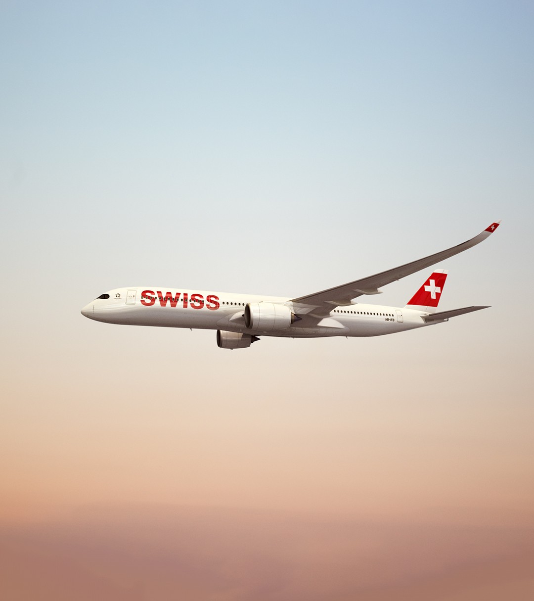 {generated} Avion SWISS volant sous un ciel d’aube doux, mettant en valeur son emblème rouge sur la dérive dans une scène épurée.