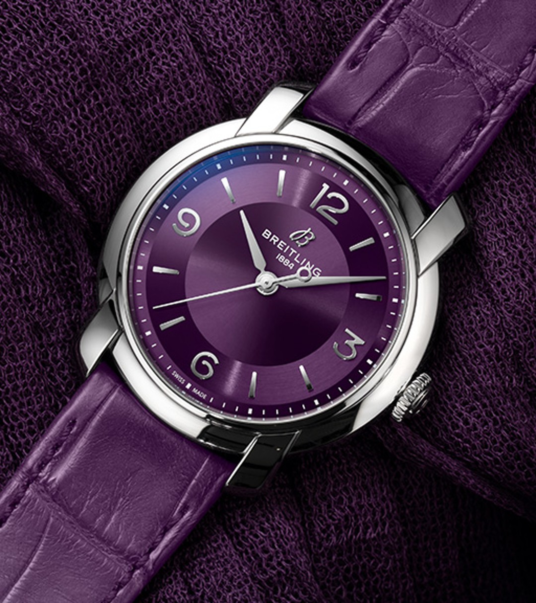 {generated} 紫の文字盤とレザーストラップを備えたBreitling Lady Premierが質感ある濃紫の布地上に映える上品な印象