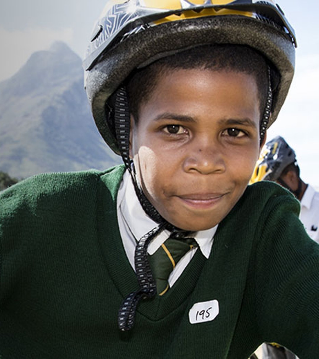 {generated} Des élèves casqués roulent à vélo en plein air dans le cadre de l’initiative Breitling x Qhubeka devant un décor montagneux.