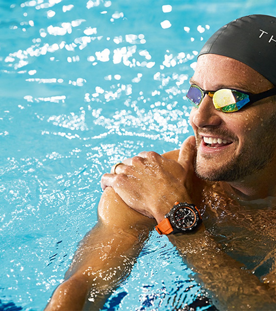 {generated} A swimmer wearing a Breitling watch with an orange strap glides through a bright pool before pausing at the water’s edge