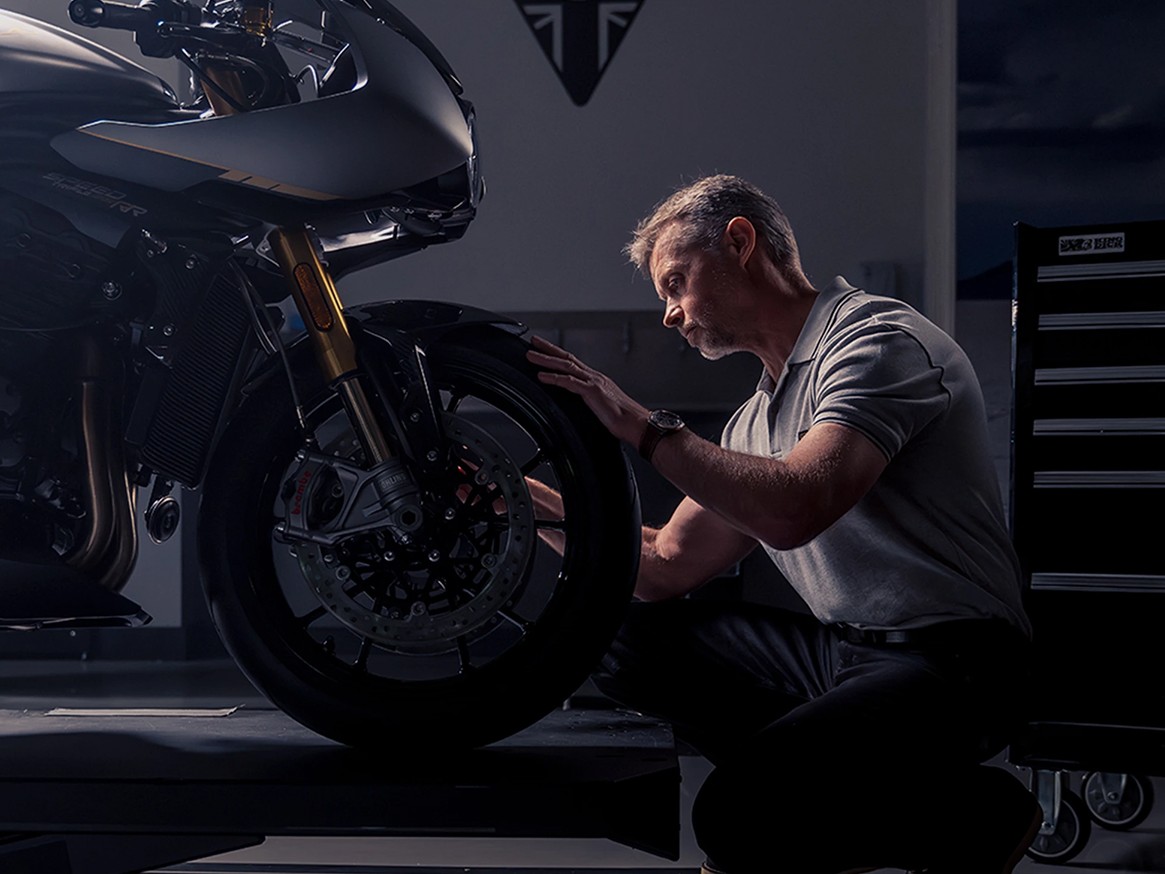Un homme portant une montre Breitling s'agenouille devant une moto Triumph