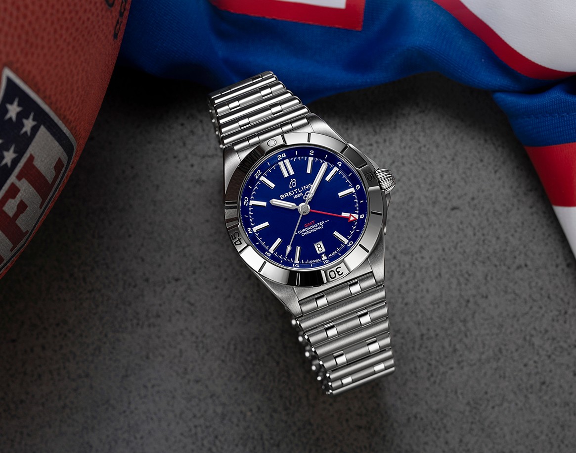{generated} Relógio Breitling de mostrador azul ao lado de itens dos New York Giants e de uma bola da NFL, destacando seu estilo esportivo.