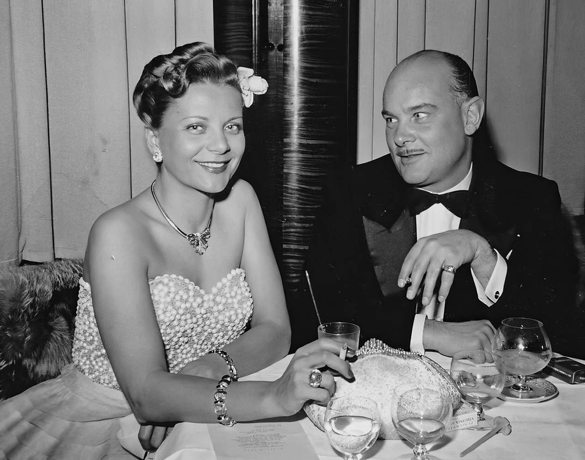 {generated} 上品なヴィンテージの男女が灯りの卓上に座り、Breitling Lady Premierのヘリテージを優雅な夜の雰囲気で表現。