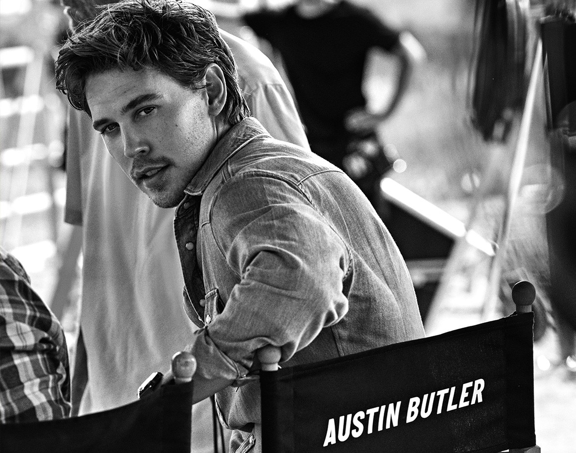 {generated} Austin Butler name on a director’s chair beside a casually dressed figure on set in a candid black‑and‑white moment