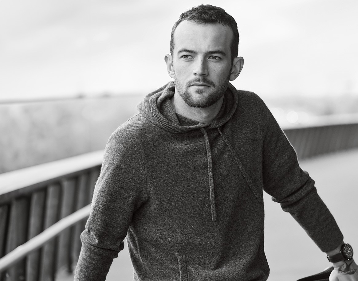 {generated} A man rests by a railing outdoors, highlighting a Breitling watch on his wrist in a calm and understated monochrome scene