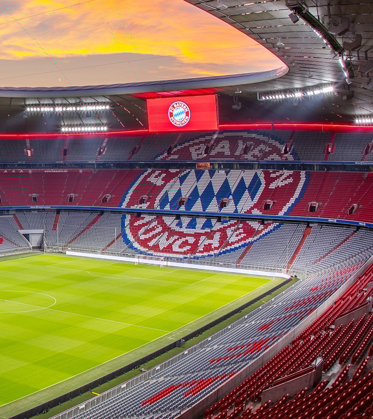{generated} 夕陽下的拜仁球場全景，空蕩看台的紅色座椅與俱樂部徽章映襯中央的綠色球場