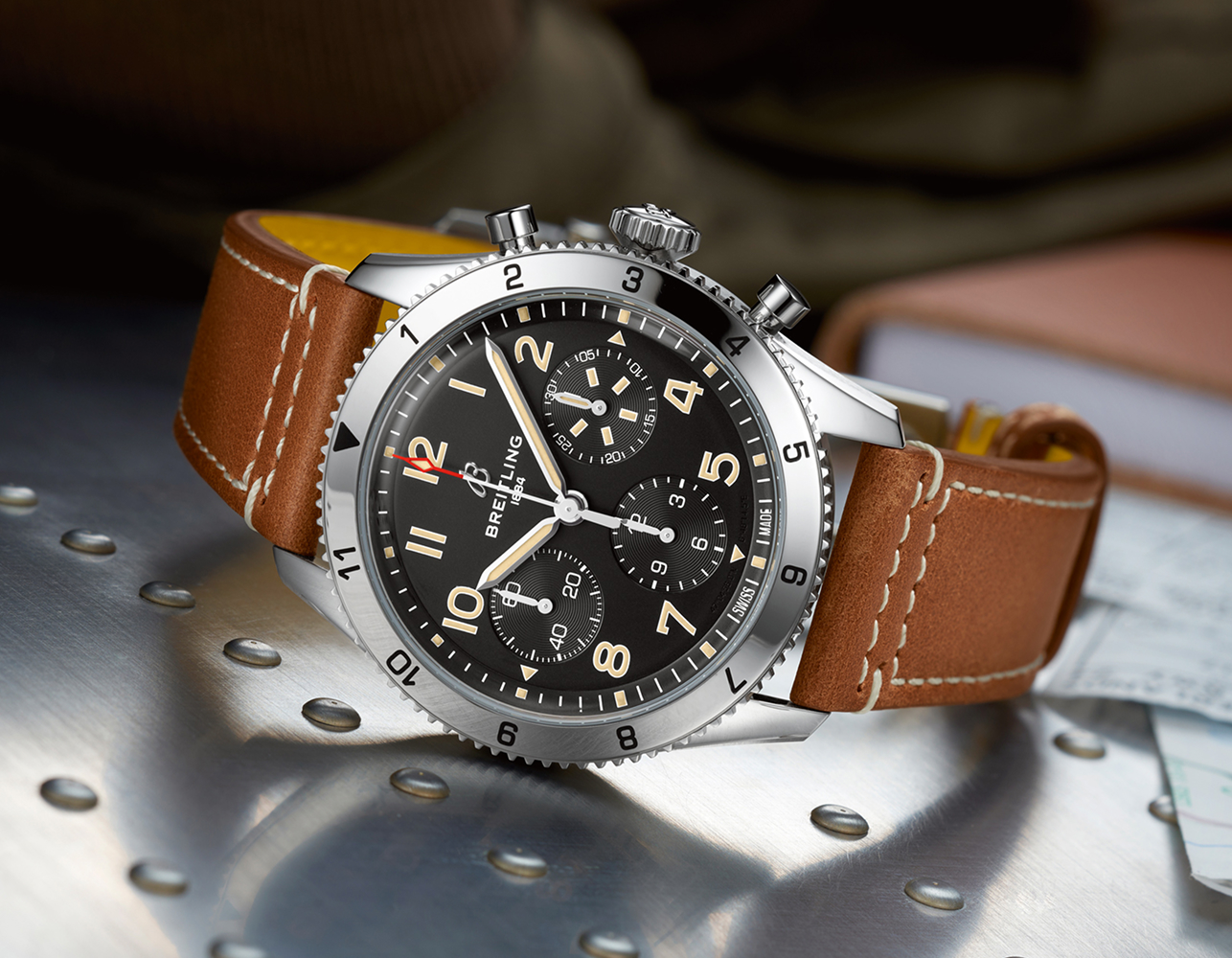 {generated} Breitling Classic AVI with black chronograph dial and brown leather strap resting on a metallic aviation surface