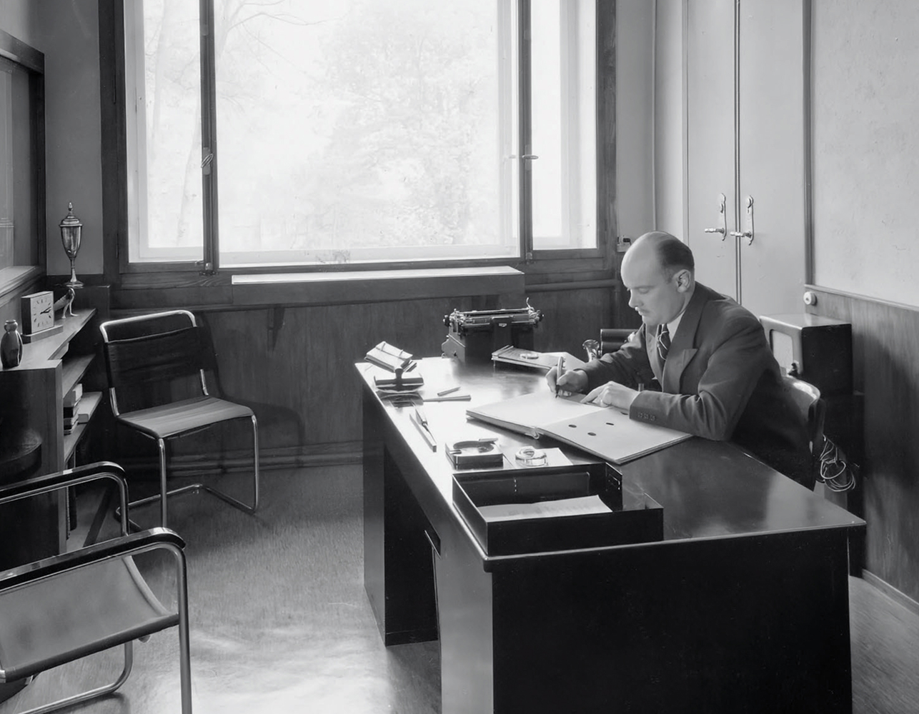 {generated} Historic office with a man writing at a tidy desk, reflecting Breitling Premier heritage in a refined, professional setting.