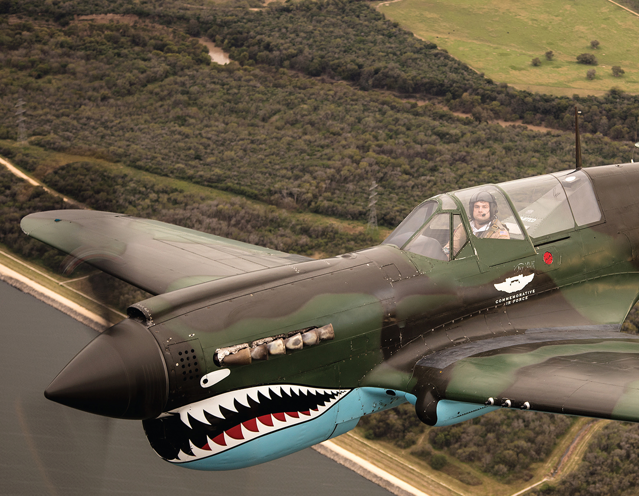 {generated} A vintage fighter plane with shark-mouth nose art flying above green terrain, reflecting the Breitling Classic Avi style