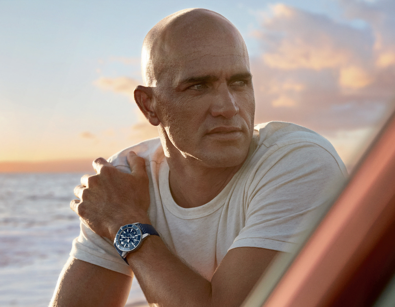 {generated} Uomo sul mare al tramonto con una Breitling Superocean dal quadrante e cinturino blu in una tranquilla scena costiera