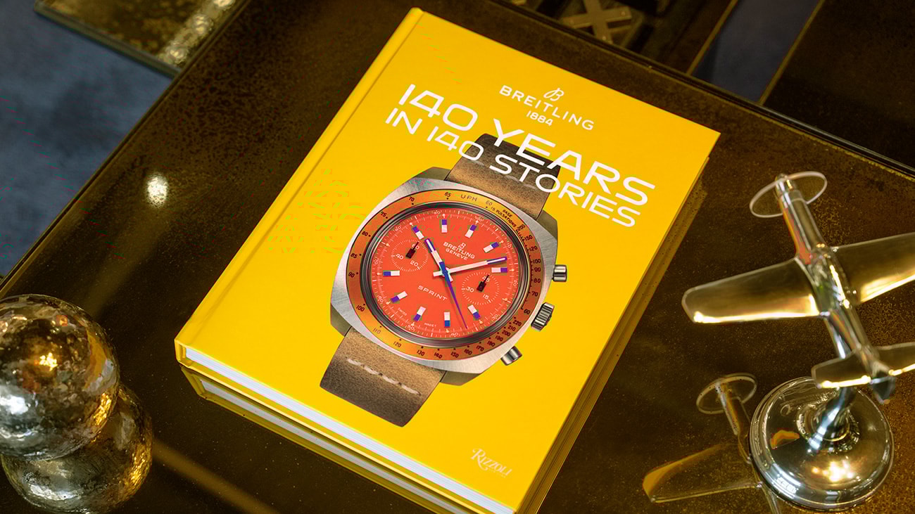 {generated} Bright yellow Breitling anniversary book on a reflective table featuring a vivid red‑dial Sprint watch for festive gifting
