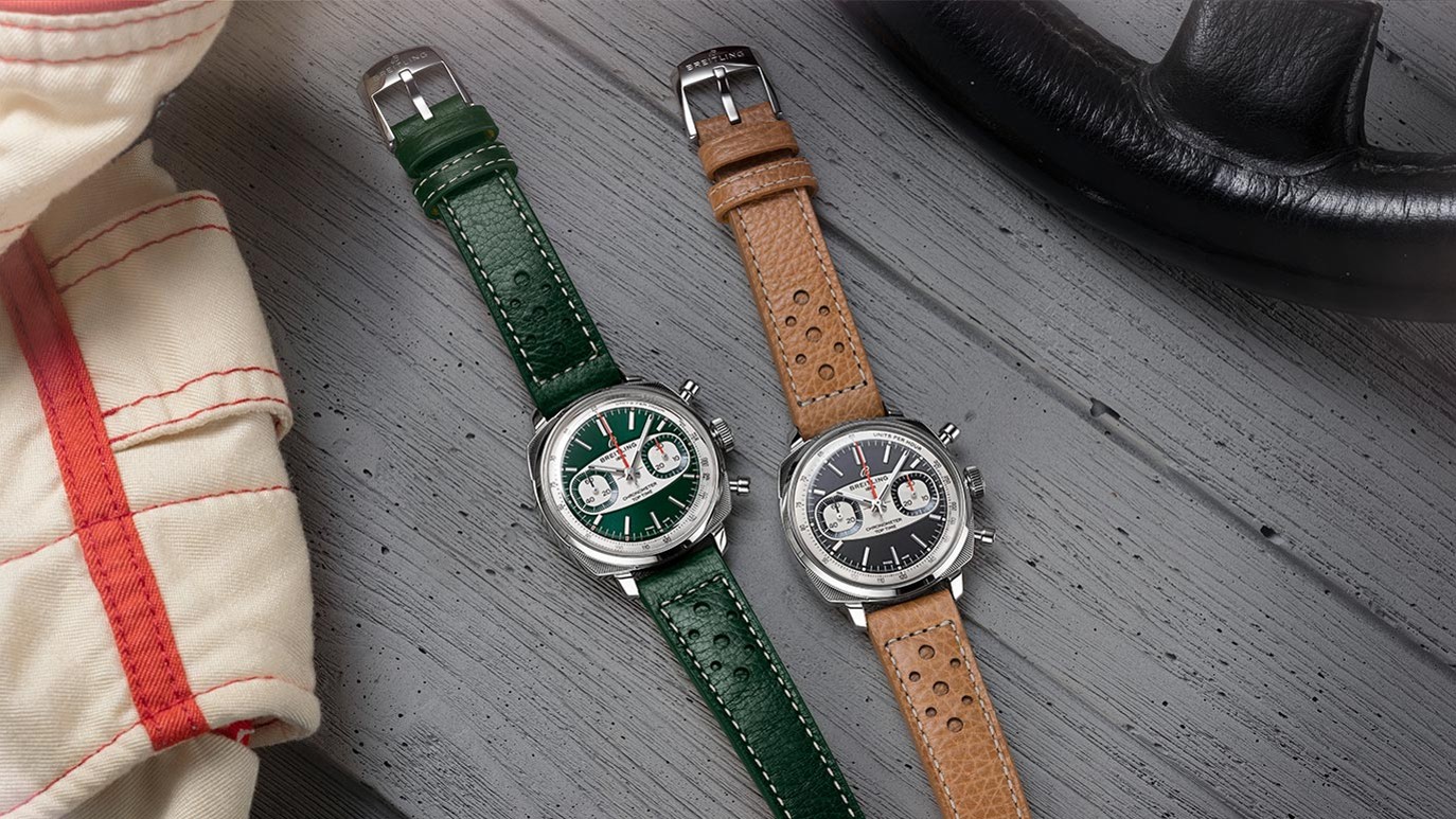 {generated} Dois Breitling Top Time Racing com braceletes verde e castanho sobre madeira cinzenta ao lado de acessórios de corrida vintage