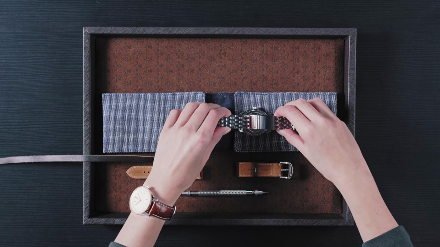 {generated} Руки регулируют металлический браслет Breitling в лотке с запасными кожаными ремешками и инструментом для замены деталей