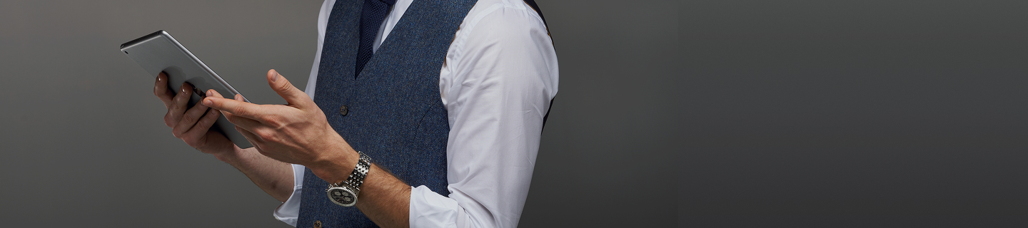 {generated} Smartly dressed advisor holding a tablet, highlighting a Breitling watch on his wrist against a refined grey background.