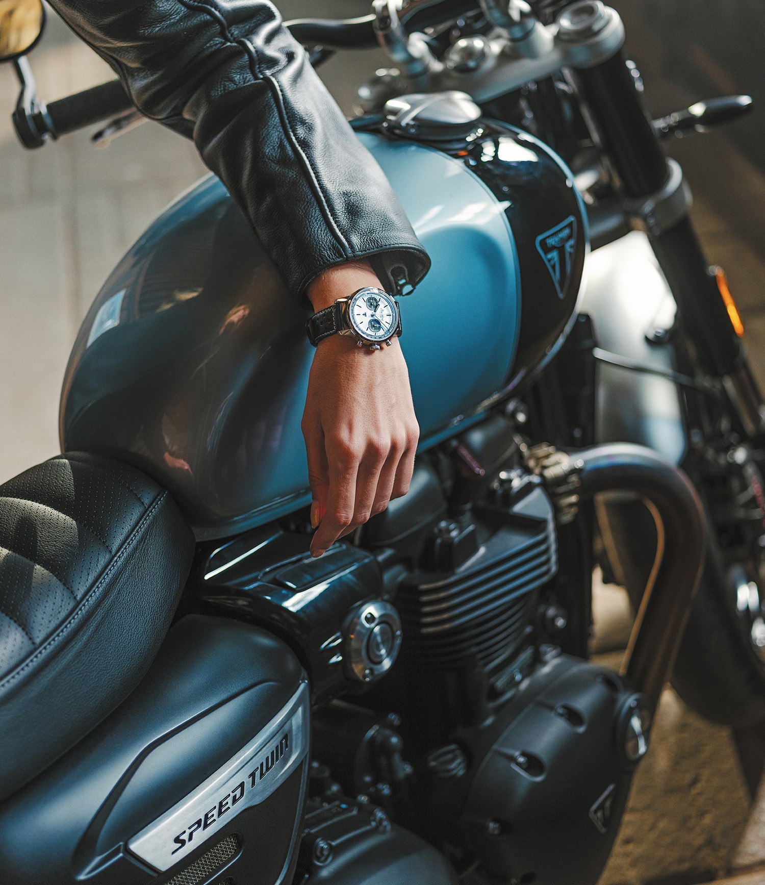 {generated} Un motard pose la main portant une Breitling Top Time Triumph sur une Triumph bleue, mettant en valeur ses détails marquants.