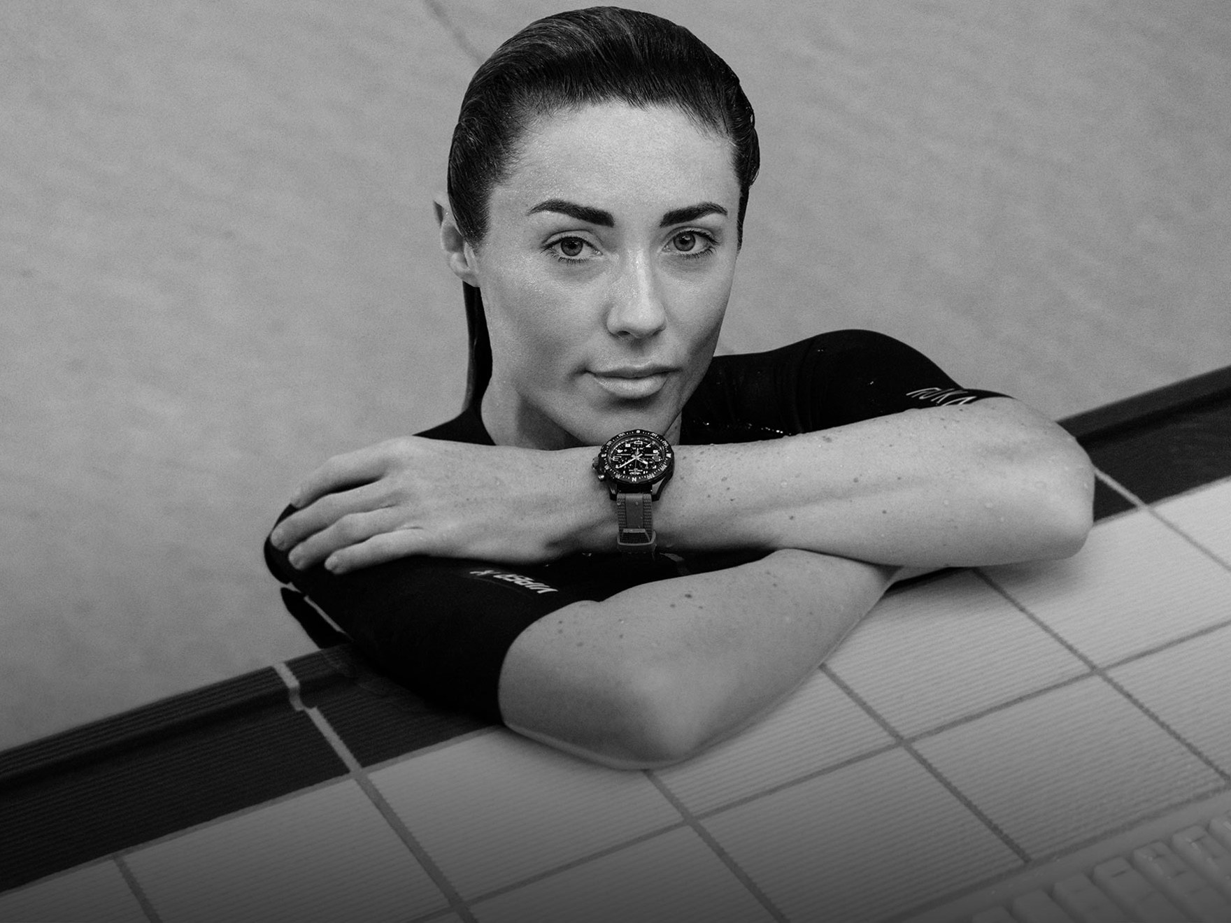{generated} Lucy Charles Barclay rests poolside with arms crossed, highlighting a Breitling sports watch against her wetsuit.
