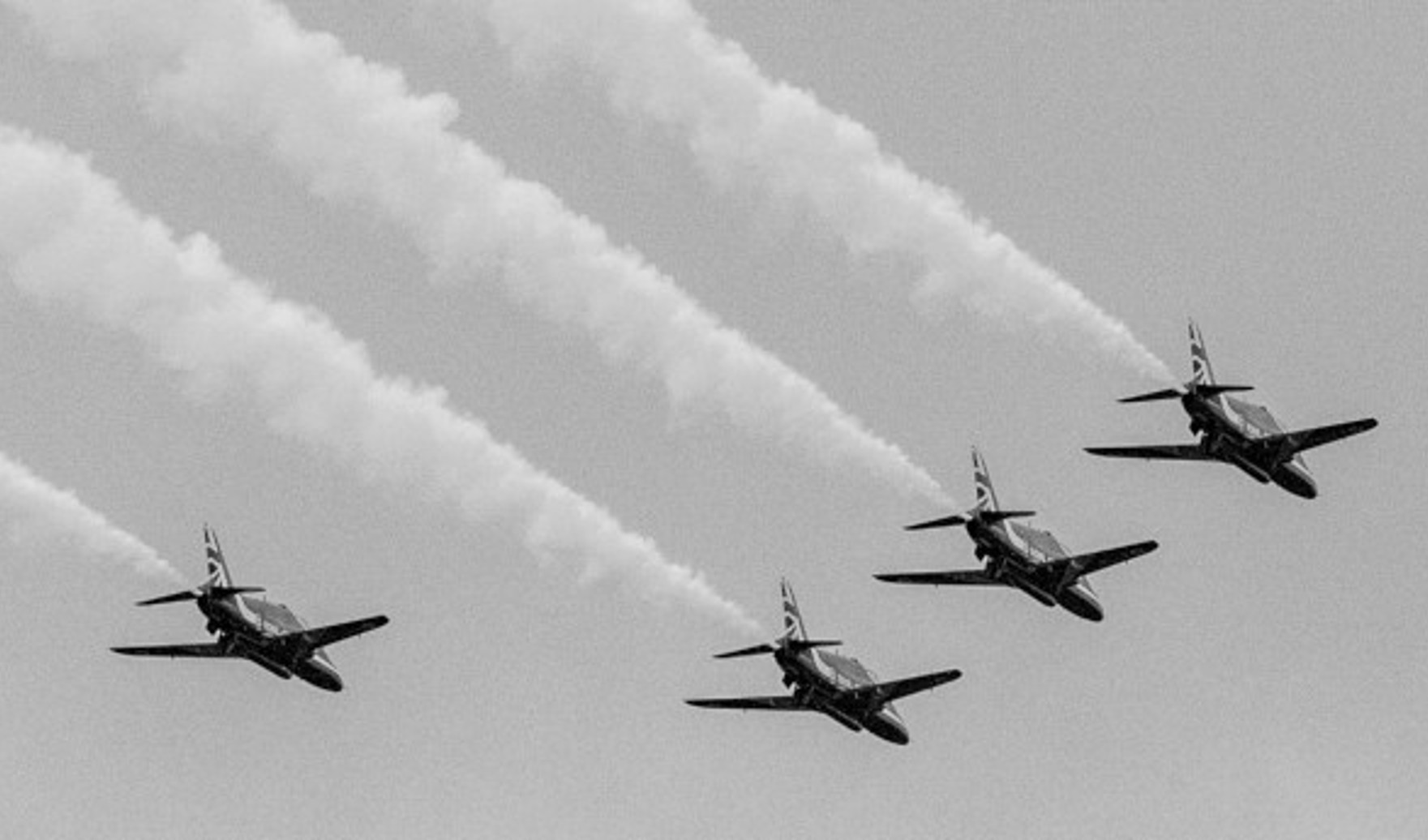 {generated} Six jets fly in tight formation, leaving white trails across a clear sky to suggest Breitling’s aviation spirit for terms content.