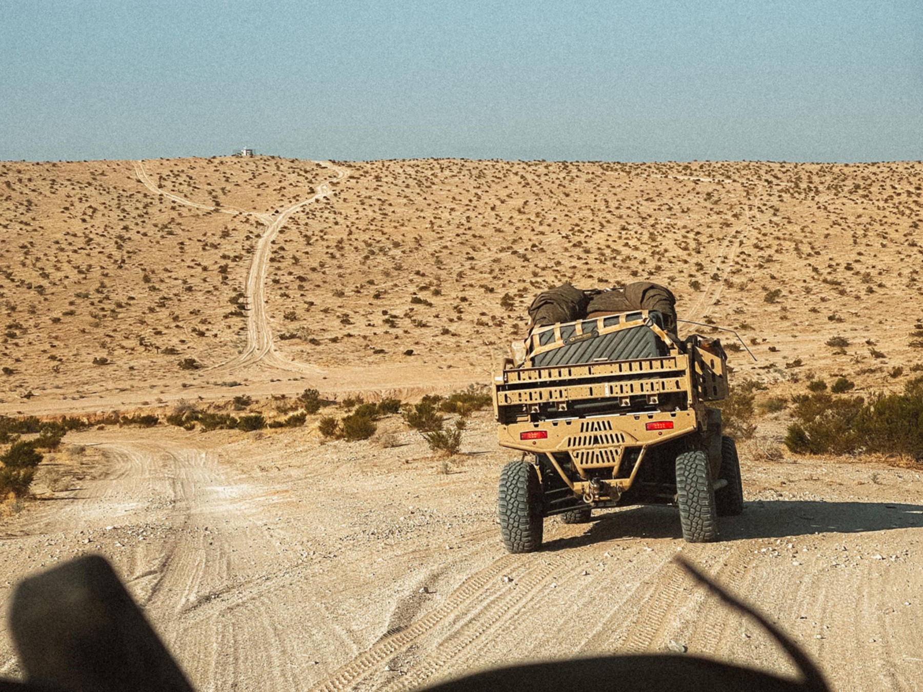 {generated} A rugged military-style vehicle travels across a remote desert trail under clear skies, evoking Breitling Emergency adventure.