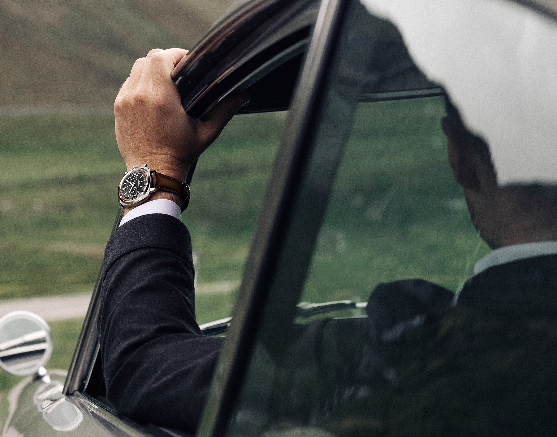 {generated} Driver wearing Breitling Top Time Tribute to Aston Martin DB5 steel and platinum watch beside classic car
