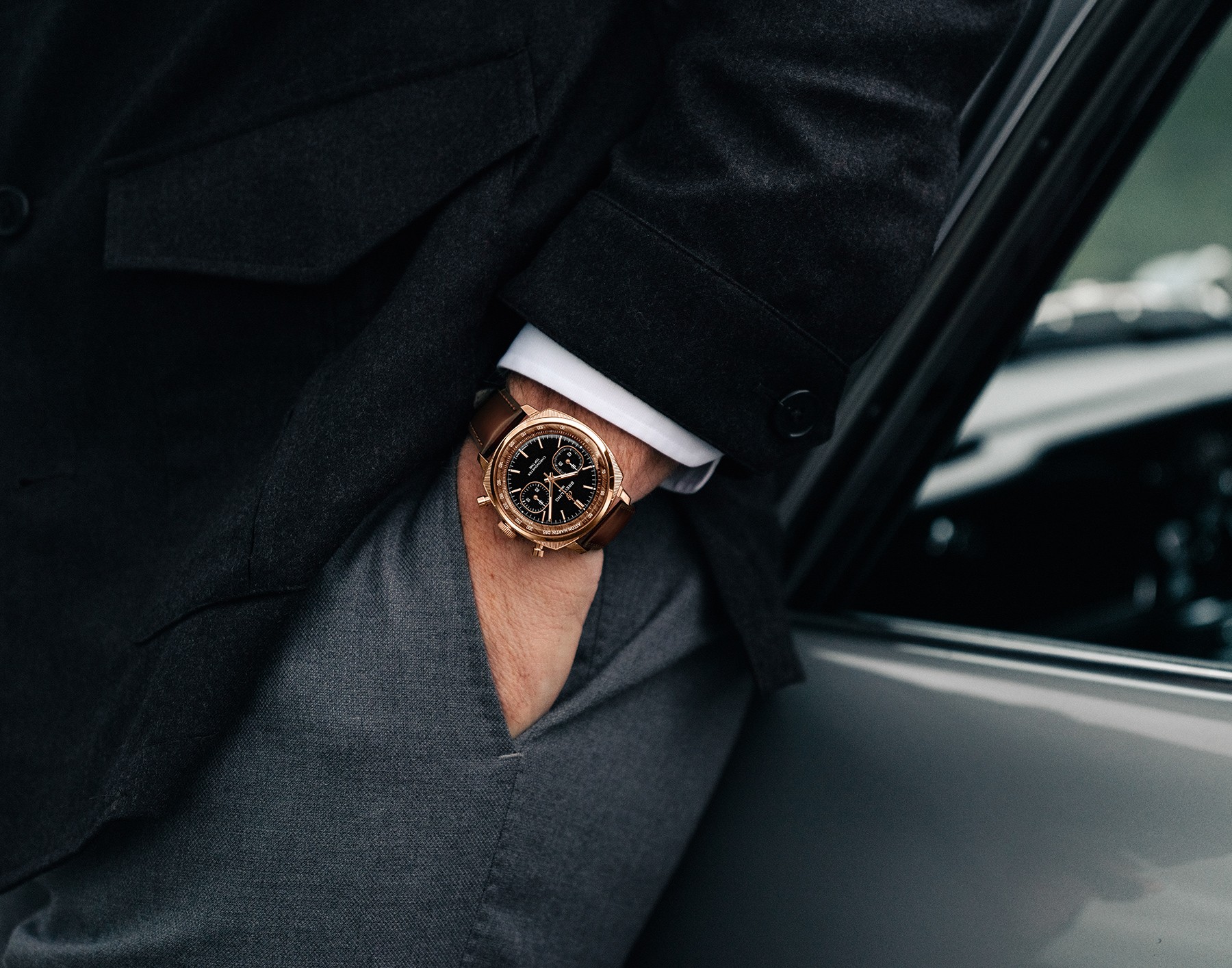 {generated} Breitling Top Time Tribute to Aston Martin DB5 in gold on brown leather strap, worn with a tailored suit