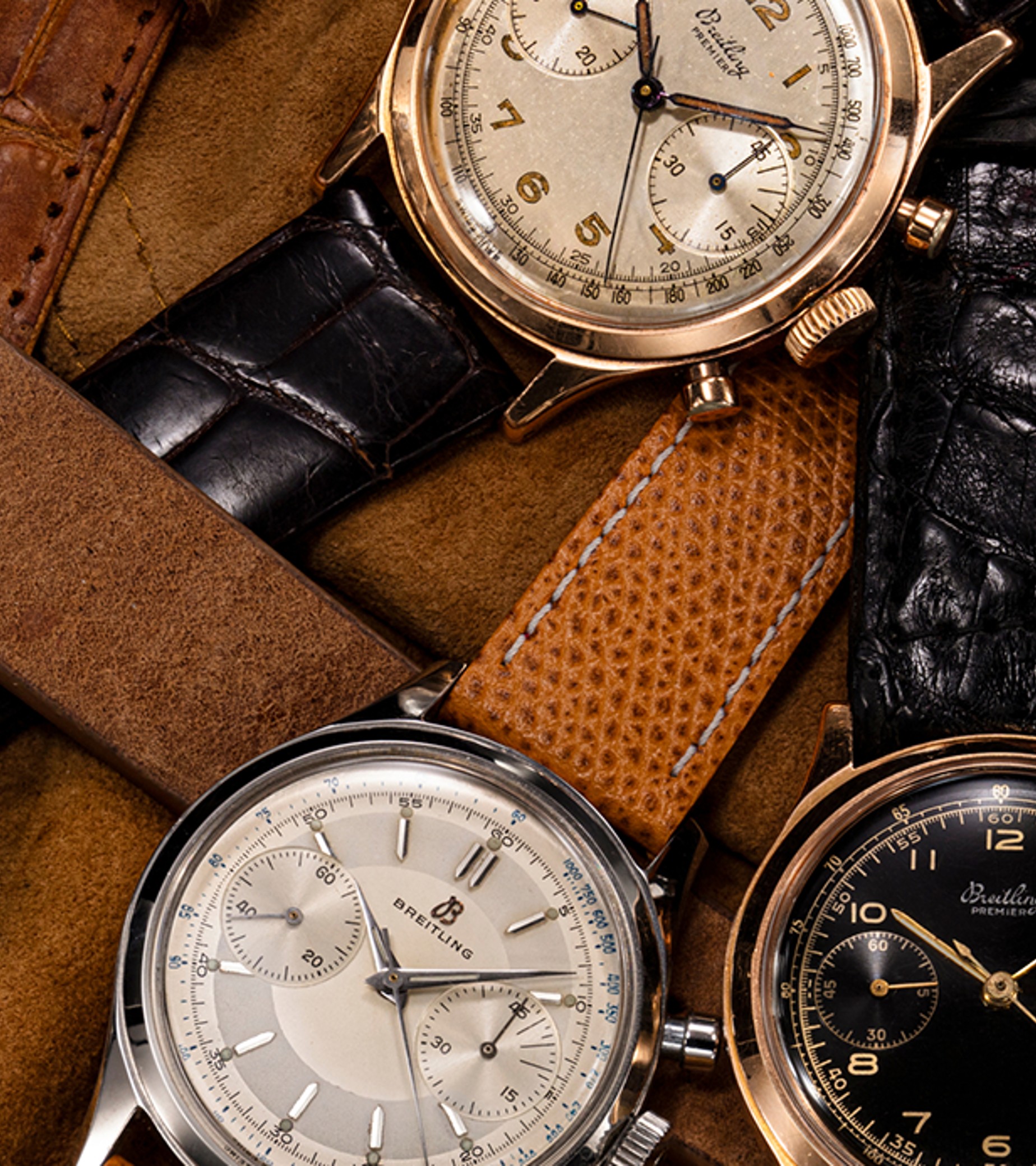 {generated} Vintage Breitling Premier chronographs arranged on soft tan fabric, showing varied dials and leather straps