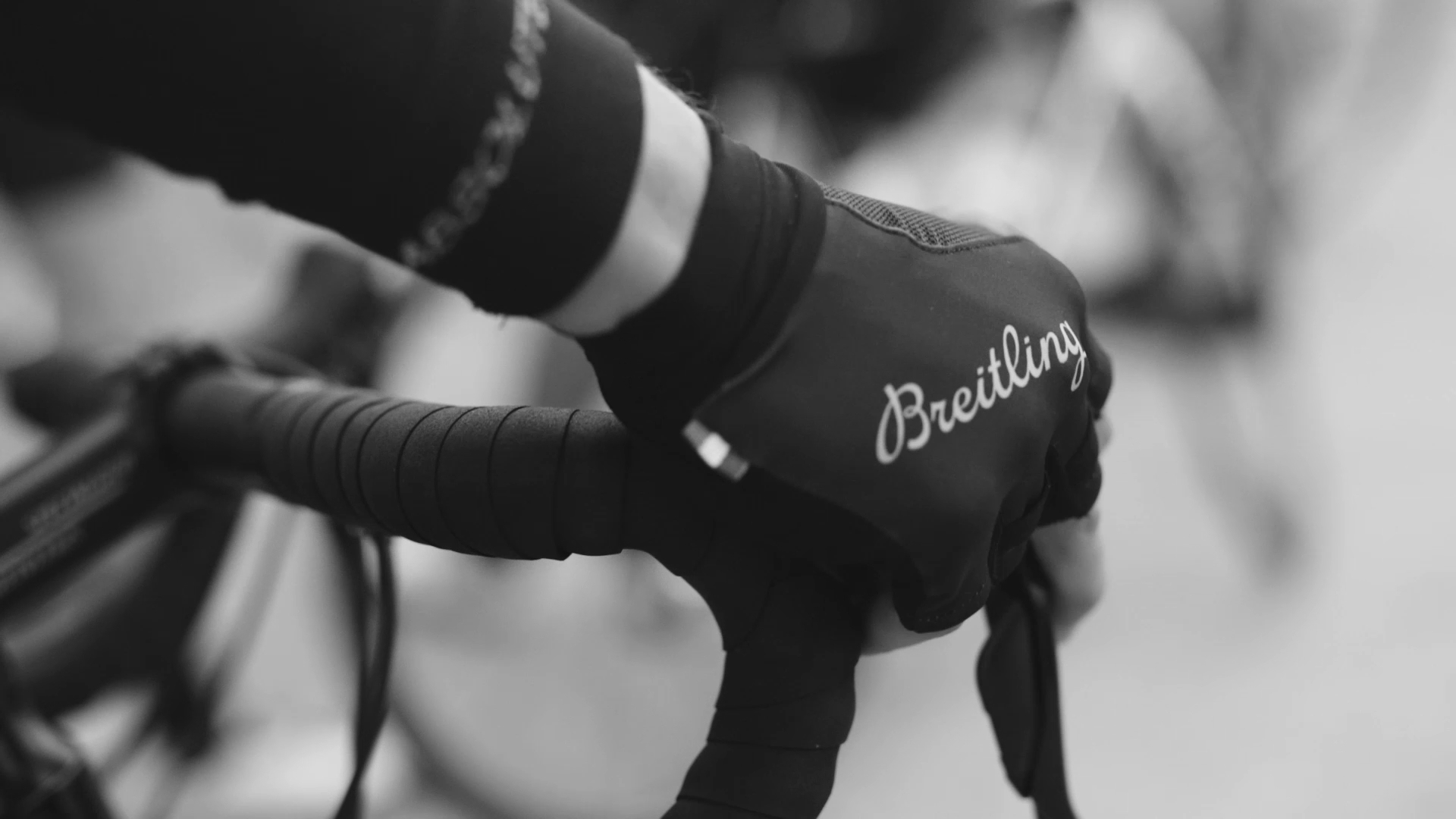{generated} Um ciclista segura o guiador com luvas Breitling, destacando o apoio da marca à iniciativa ciclística Qhubeka.