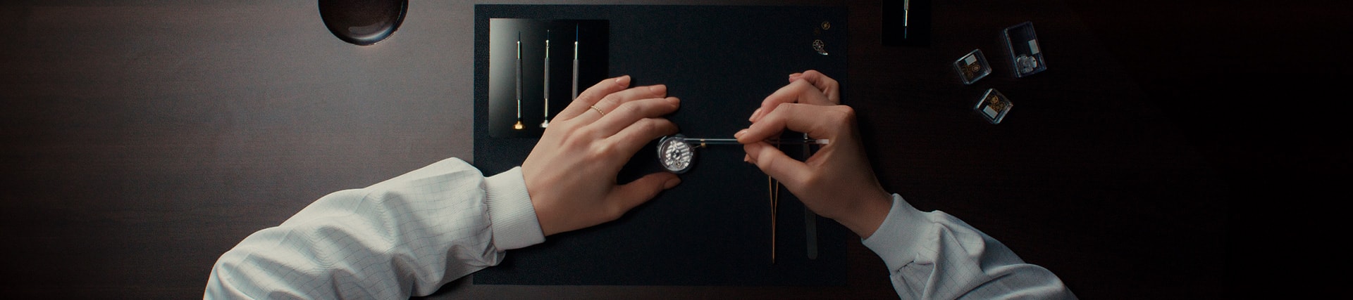 {generated} Watchmaker delicately services a Breitling movement on a dark workspace with precision tools arranged for meticulous care