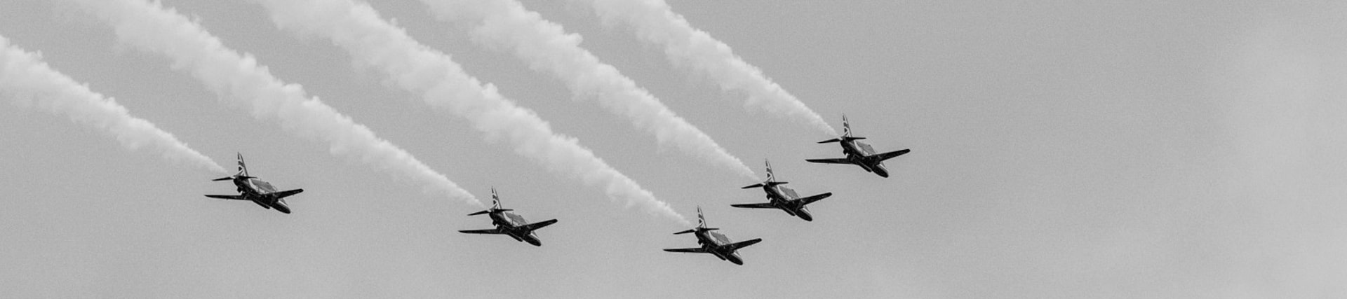 {generated} Six jets fly in tight formation, leaving white trails across a clear sky to suggest Breitling’s aviation spirit for terms content.