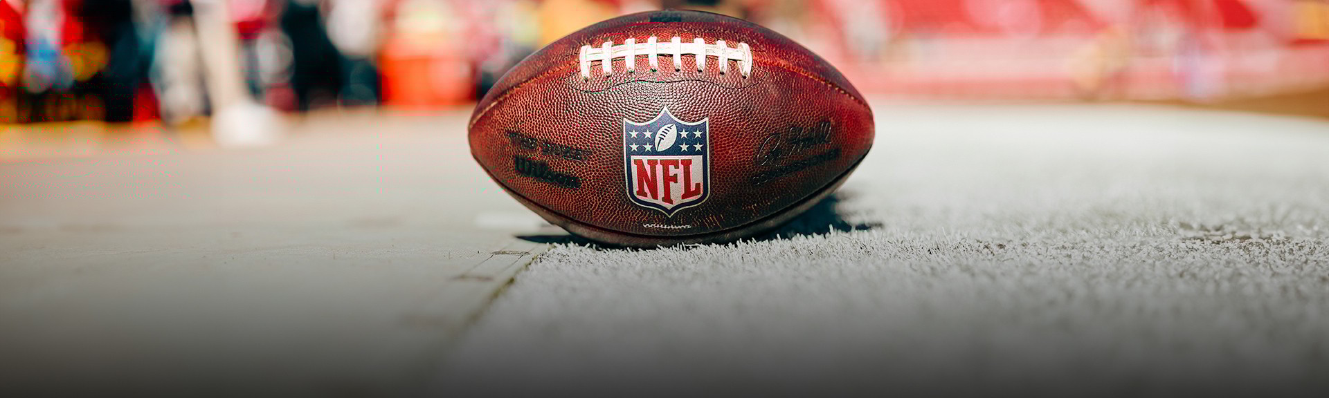{generated} Uma bola da NFL no campo destaca a cena do estádio, ressaltando o anúncio da parceria com a liga.