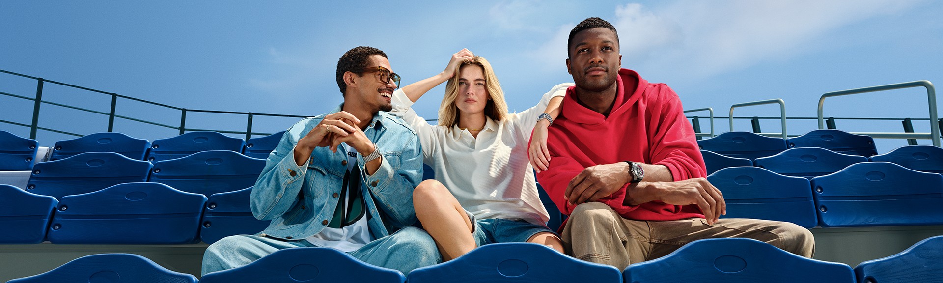 {generated} Three friends relax in bright blue stadium seats, each showcasing a Breitling watch in a casual NFL-inspired setting.
